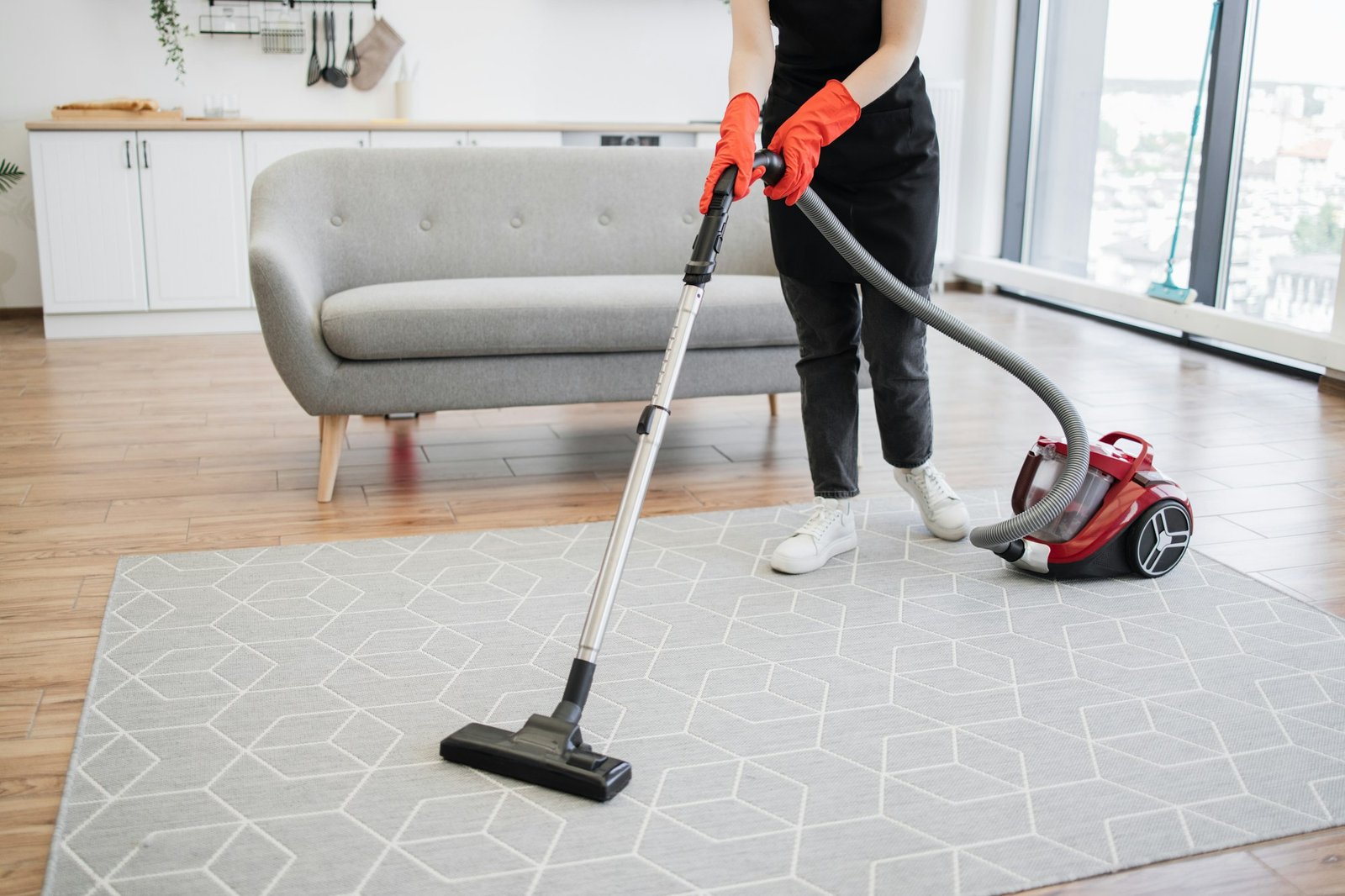 Cropped view of hands of woman cleaning service worker vacuuming carpet.